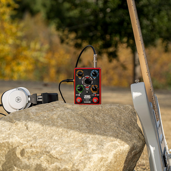 POD Express Guitar and headphones on a rock outdoors with a guitar leaning against the rock